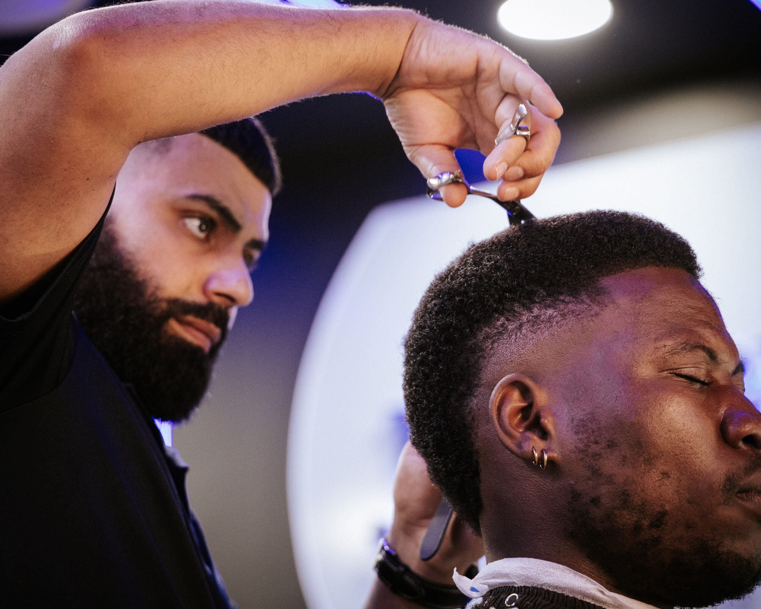 A barber is expertly trimming the top of a client's hair, showcasing a stylish fade and well-groomed appearance.